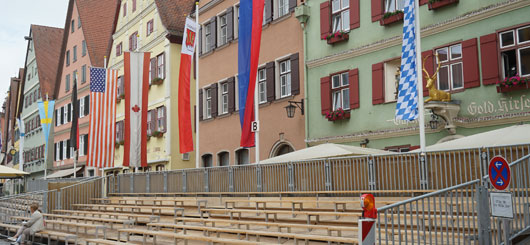 Ein buntes Fahnenmeer dominiert das Straßenbild. Eine große Ehrentribüne für die Prominenz.